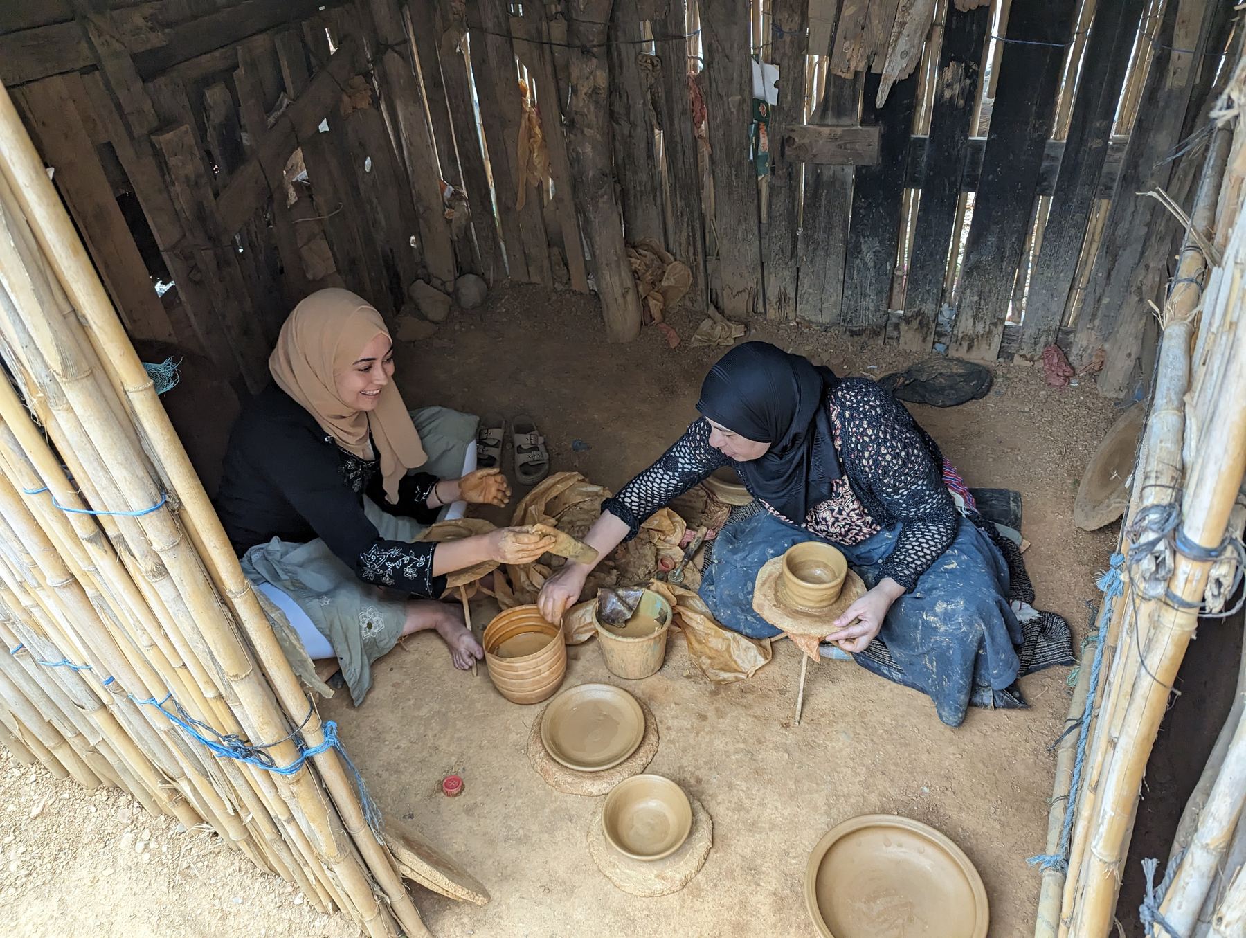 Two local women shaping pottery together inside a traditional nouala